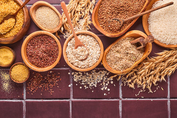 White, brown and red rice, buckwheat, millet, corn groats, quinoa and bulgur in wooden bowls on a brown stone kitchen table. Gluten-free cereals. Top view with copyspace