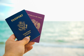 a hand holding two passport a red and a blue one on a beach