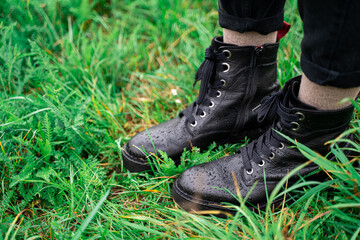Young woman wearing black leather warm wet boots standing on green fresh grass in forest or park on rainy cloudy early autumn september or october day. Holiday, leisure, lifestyle and fashion