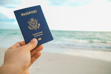 a hand holding a blue passport on a beach