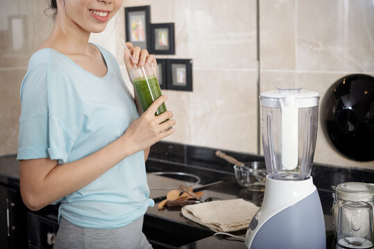 Cropped image of positive healthy young woman drinking green smoothie while being on detox diet