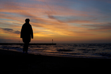 Fototapeta na wymiar Silhouette of a vacationer walking on the beach in Kolobrzeg on the Polish Baltic coast after sunset 