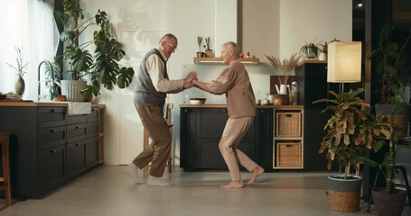 Faithfulness concept. Happy sweet 65-70 senior man and woman have fun dancing together, laughing in cozy house kitchen.