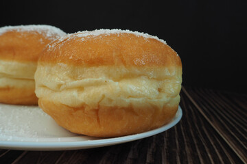 two doughnuts sprinkled with powdered sugar lie on a plate on a dark background . side view