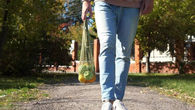 Woman walks with a braided string bag of fresh fruit. Life without plastic waste. Low-waste lifestyle. Sustainable ecological lifestyle