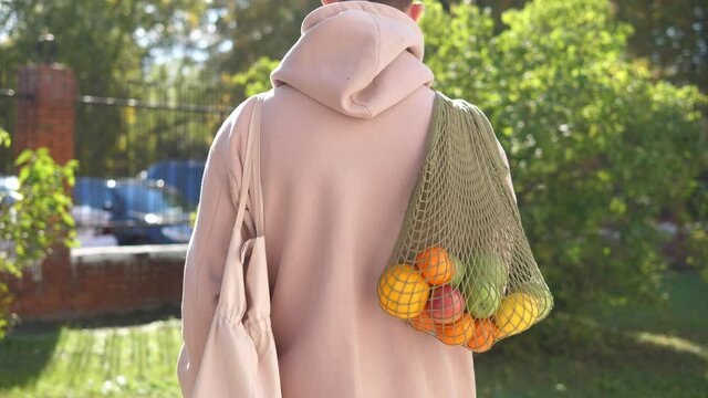 Woman walks with a braided string bag of fresh fruit. Life without plastic waste. Low-waste lifestyle. Sustainable ecological lifestyle