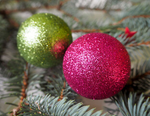 close pink and green shiny Christmas toys are lying on the branches of the Christmas tree . side view