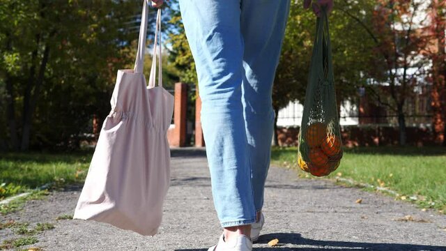 Woman walks with a braided string bag of fresh fruit. Life without plastic waste. Low-waste lifestyle. Sustainable ecological lifestyle