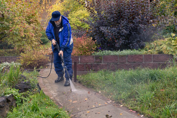 A man washes a garden path with a high pressure washer. Autumn work in the garden.