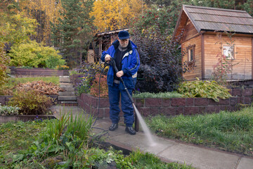 A man washes a garden path with a high pressure washer. Autumn work in the garden.