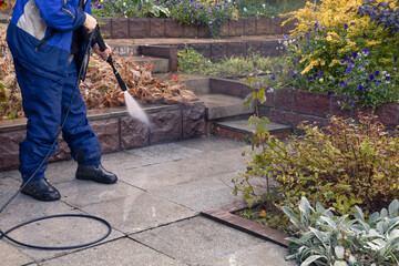 A man washes a garden path with a high pressure washer. Autumn work in the garden.