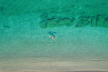 Young woman in a swimsuit swimming in sea water on the beach. View from above. Top, drone view