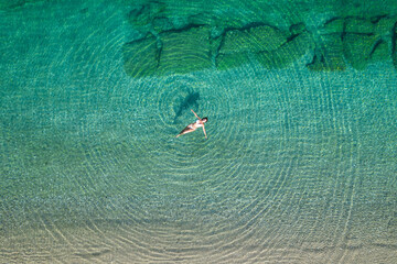 Young woman in a swimsuit lying on sea water on the beach. View from above. Top, drone view