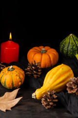 Close-up of green and orange pumpkins, with autumn leaves, pine cones and burning orange candle, selective focus, on dark wooden table, vertical, with copy space