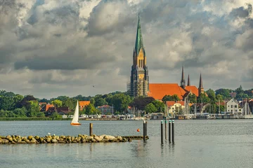 Foto op Canvas A sailboat sails in the Schlei cove under the bell tower of the Schleswig Cathedral, St. Peter's Cathedral in Schleswig soars. Holstein, Schleswig-Holstein, Germany, Europe © Guido Paradisi