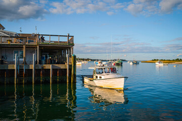 Fototapeta premium Calm morning seascape with a white fishing trawler launching to the sea from the commercial dock in Chatham Pier harbor
