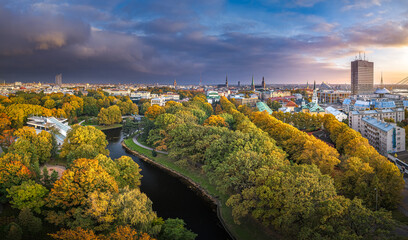 Park in Riga with trees in autumn colors. Colorful sunset over the city panorama. Downtown in background.