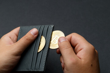 Fototapeta premium A person holds Bitcoin coins. A businessman puts bitcoin gold coins into a wallet. Bitcoin purchase concept. Bitcoin and wallet. Bitcoin Conservation. Cryptocurrency. Close-up. Virtual money