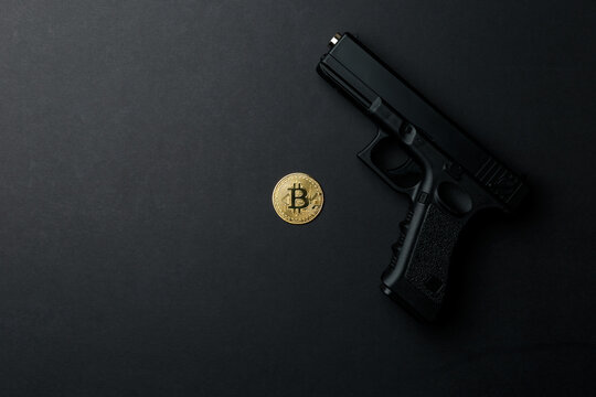 A gold bitcoin coin next to a gun on a black background. Bitcoin Conservation. Cryptocurrency. Close-up. Virtual money. Copy space. The concept of the shadow economy