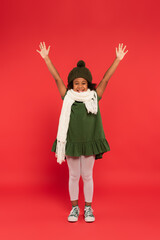 African american kid in warm hat and knitted hat waving at camera on red background