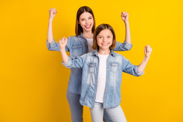 Photo of pretty strong siblings dressed denim shirts rising fists smiling isolated yellow color...