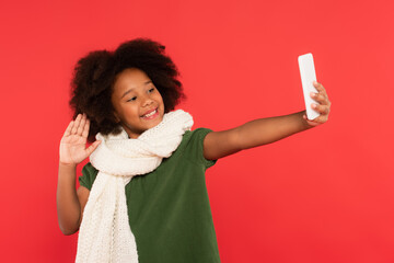 African american kid in warm scarf having video call on cellphone isolated on red