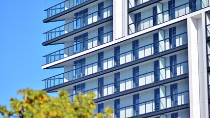 Inspiring view of the modern city. The wall of the apartment building   against trees. Apartment construction and ecology, view of  modern  building with blue sky and green tree. Sunlight