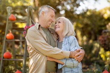 Happy loving senior spouses embracing, walking in garden and enjoying warm autumn days, spending time outdoors