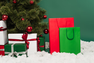 Presents near shopping bags, decorative snow and christmas tree on green background