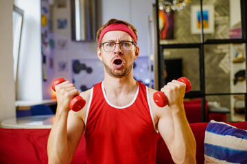 Funny man exercising and doing sport training with small dumbbells in living room.