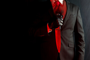 Portrait of Businessman in Black Suit and Red Tie Holding Bloody Red Knife on Black Background. Halloween Horror Movie Killer Concept. 