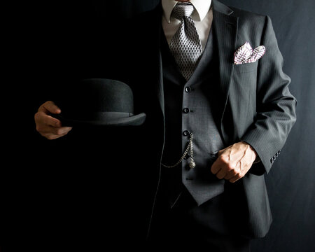 Portrait of Man in Dark Suit Holding Bowler Hat on Black Background. Vintage Style and Retro Fashion of Classic British Gentleman.