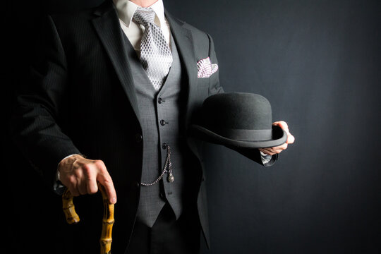 Portrait of Man in Dark Suit Holding Bowler Hat and Umbrella on Black Background.. Vintage Style and Retro Fashion of Classic English Gentleman.