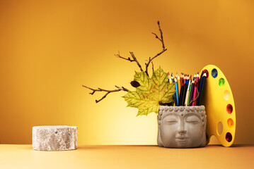 Creative yellow background with geometric podium for product presentation or exhibitions. Still life from the Head of Buddha and and watercolors and pencils.