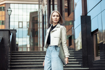 Stylish modern business woman with a laptop in her hands on the steps near the business center. Lifestyle