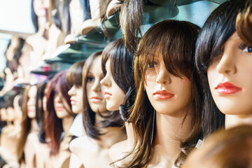 Women's wigs are put on the shelf in a wig shop. - obrazy, fototapety, plakaty