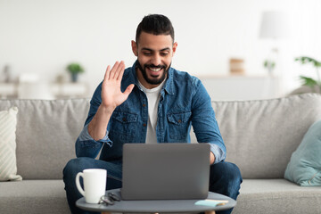 Online meeting. Happy young Arab man using laptop computer for conferencing, having video call at home