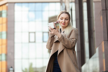 Fototapeta premium Beautiful blonde woman applies makeup with a brush in city