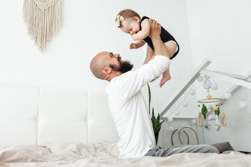 Caring father plays with his little daughter on the bed in bedroom. Love and care, happy family, spending time together concept