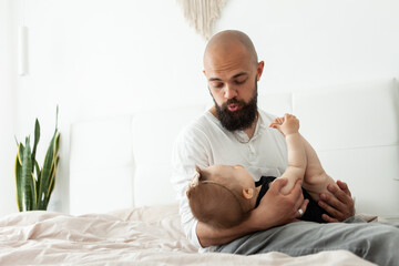 Caring father plays with his little daughter on the bed in bedroom. Love and care, happy family, spending time together concept