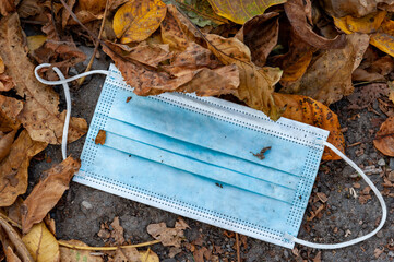 Discarded face mask seen lying as garbage on ground in autumn leaves.