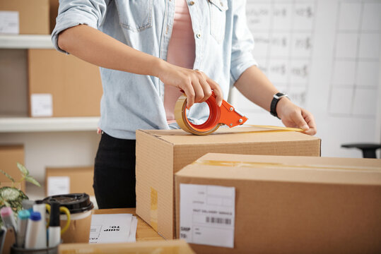 Close-up of unrecognizable woman standing at table with packages and taping parcel box before delivery