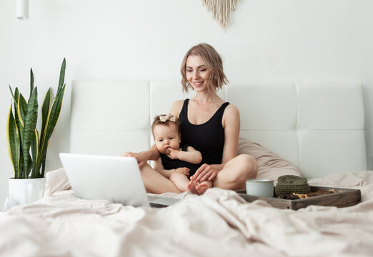 Cute mother with her little daughter is watching a video or movie in laptop and having breakfast in bed. Happy family. Spend time together. Love and care