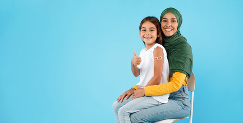 Vaccinated Muslim Mother And Little Daughter Gesturing Thumbs-Up, Blue Background
