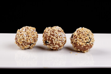 Beautiful candies with sesame seeds on a white plate on a black background