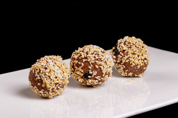 Beautiful candies with sesame seeds on a white plate on a black background