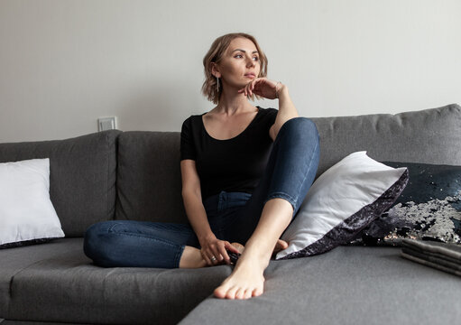 Woman Sits On A Sofa With A TV Remote Control And Looks To The Side