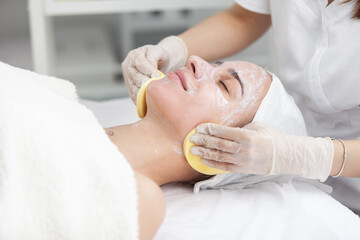 Fototapeta na wymiar Facial massage and skincare treatment. Dermatologist hands cleaning relaxed serene young woman face with pads in beauty salon during skincare treatment. Face massage