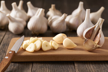 Chopped garlic on a cutting board,  in background a pile of garlic unpeeled.
