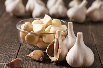 Organic garlic cloves and bulbs in a glass bowl with peeled garlic on a wooden table.